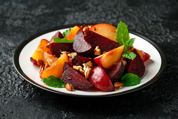 Vegan Plum, beet salad with pecan nuts, mint and herbs on rustic black table