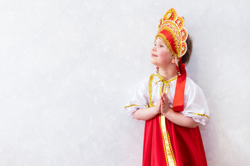 Fototapeta na wymiar Girl 5 years old in a red dress and kokoshnik. A sweet smile on his face and holds his hands on his chest. National traditional Russian clothes.