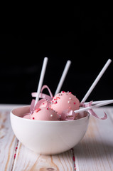 Delicious dessert cake pops in pink milk chocolate in white piala on a wooden background.