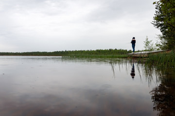 Fototapeta na wymiar Finnish young woman fishing on the lake in a rainy day.