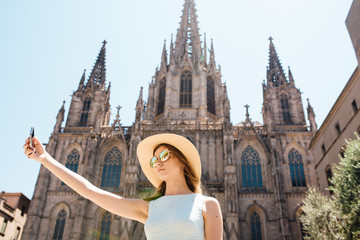 Fototapeta premium Young and happy tourist woman making selfie photo in front of cathedral in Barcelona