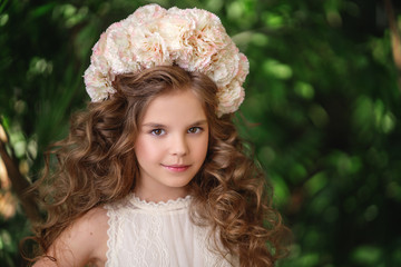 Portrait of a 7 years old girl with a voluminous curly hairstyle and a wreath of flowers on her head. She is looking into the frame and smiling.