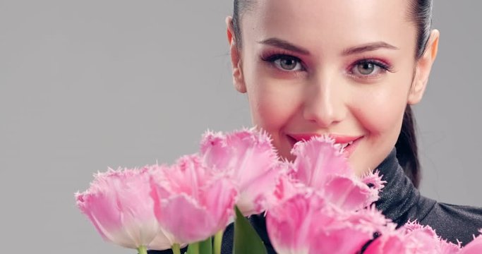 Beautiful smiling girl with flowers. Happy brunette girl with big bouquet flowers of  pink tulips. Smiling face of young beautiful woman with a healthy clean skin. Woman with bright makeup.