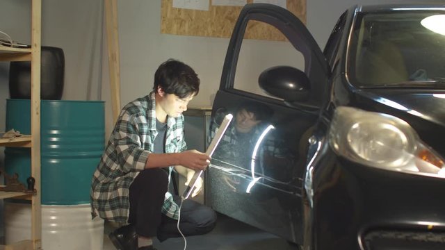 Mechanic inspects car door with ultraviolet lamp