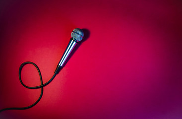 Silver microphone on a red background, with a black cord.