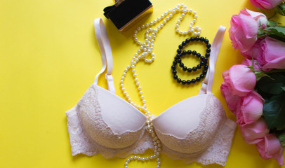 Flat lay of woman fashion accessories, underwear, bouquet of roses, parfume, jewelry, on yellow background. Concept of fashion, magazines, social media. Top view pink lace lingerie