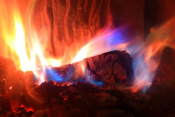 Płomienie z palącego się drewna w kominku w kolorze złotym, czerwonym i niebieskim.