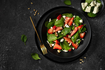 Top view of a black plate with healthy strawberry spinach salad