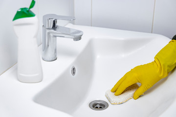 Girl is cleaning a sink in the bathroom, using clean water using yellow gloves and a white sponge.