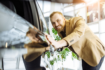 young caucasian guy examining all details of new car in dealership, before buying it. cars,...