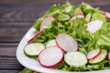 Fresh and delicious salad with lettuce, radish, cucumbers and olive oil in a white bowl, with table offerings