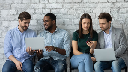 Focused diverse young people sit in queue discuss ideas work on laptops together, concentrated...