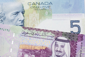 A close up macro shot of a blue five Canadian dollar bill with a five Saudi riyal note