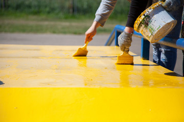 Yellow paint is applied to the surface. The painter does the work. Application of a coat of paint. Sunny day. Bright yellow color.