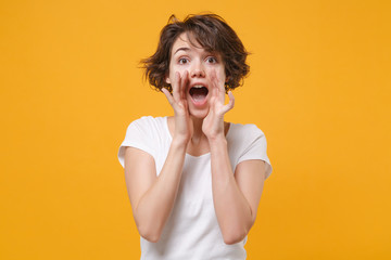 Excited young brunette woman girl in white t-shirt posing isolated on yellow orange wall background studio portrait. People lifestyle concept. Mock up copy space. Scream with hands gesture near mouth.