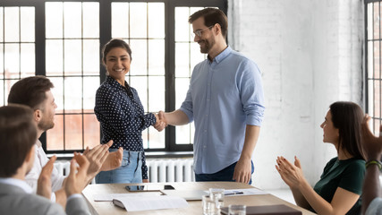 Smiling businessman shake hand of overjoyed Indian female newcomer at office meeting, diverse colleagues applaud to male employer handshake excited biracial woman worker, greeting with job promotion