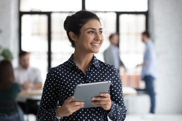 Smiling young Indian female employee hold tablet look in distance thinking, happy millennial biracial woman worker distracted from pad gadget, lost in thoughts visualizing, business vision concept - Powered by Adobe
