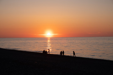 Fototapeta premium Sunset on the black sea. People walk along the beach and pier. Quiet, calm evening.