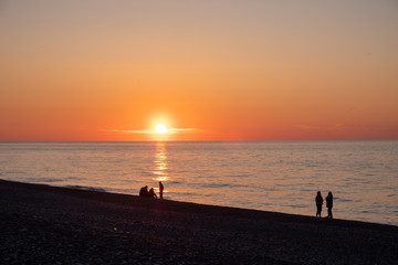 Fototapeta premium Sunset on the black sea. People walk along the beach and pier. Quiet, calm evening.