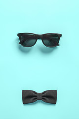 Black stylish sunglasses and bow tie on blue background. Flat lay. Minimal style concept