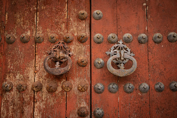 Fototapeta premium antique rusty door knockers of an ancient red wooden door