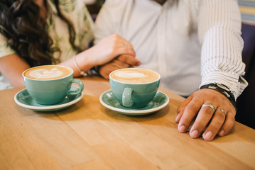 Cups of coffee on a background of visitors.
Cups of coffee on a table in an institution.
Hands of people and coffee. Loving couple holding hands, cuddling