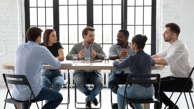 Diverse multiracial businesspeople sit at desk in office brainstorm discuss business ideas together, concentrated multiethnic colleagues gather in boardroom negotiate at meeting or briefing