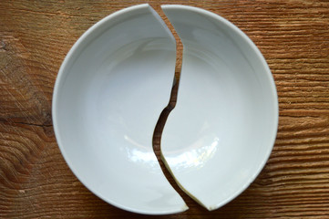 Broken white ceramic bowl on wooden background