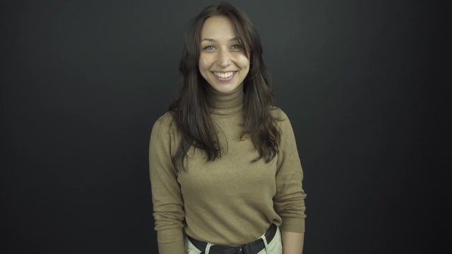 excited brunette in brown turtleneck smiles and shakes hands