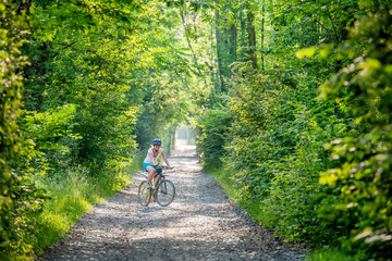 Woman rides bicycle in the beautiful green forest.
