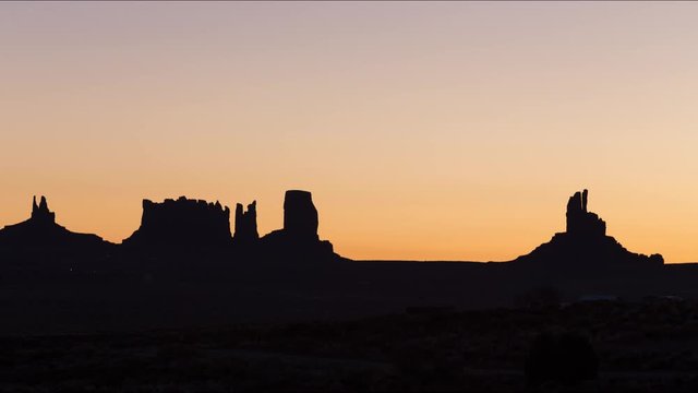 A long-lens timelapse looking into Monument Valley as the sun starts to illuminate the sky and the silhouetted mesas.
