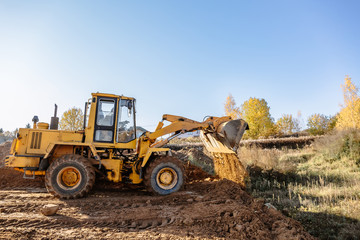 Fototapeta premium large yellow wheel loader aligns a piece of land for a new building. Preparation of the land for the auction. Leveling the landscape and adding sand for construction.