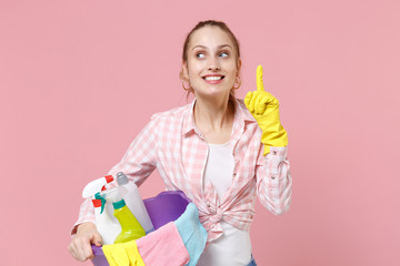 Pensive woman housewife in rubber gloves hold basin with detergent bottles washing cleansers doing...