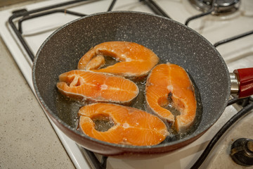 A steak of delicious fish varieties is fried in a frying pan on a kitchen gas stove