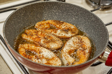 A steak of delicious fish varieties is fried in a frying pan on a kitchen gas stove