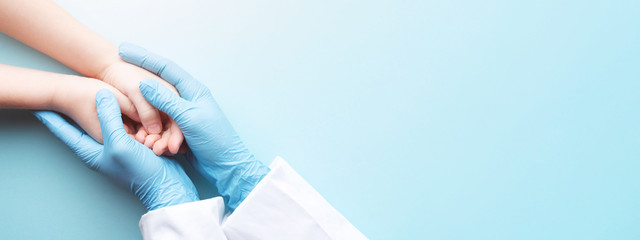 Die Hände des Arztes in Handschuhen, die die Hände des Kindes halten. Medizinische Fahne mit Kopienraum auf blauem Hintergrund. Pflegekonzept.