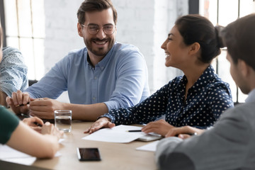 Smiling diverse businesspeople gather at desk in office have fun joke discussing ideas together, happy multiethnic colleagues laugh negotiate brainstorming at meeting in boardroom, teamwork concept