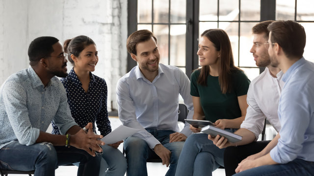 Happy multiracial young people sit in circle in office have fun discussing business ideas together, smiling diverse multiethnic colleagues engaged in teambuilding activity, teamwork concept