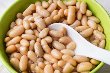 White backed beans and ceramic spoon in a green bowl. Bean is source of vegetable protein and ingredient for vegetarian food.