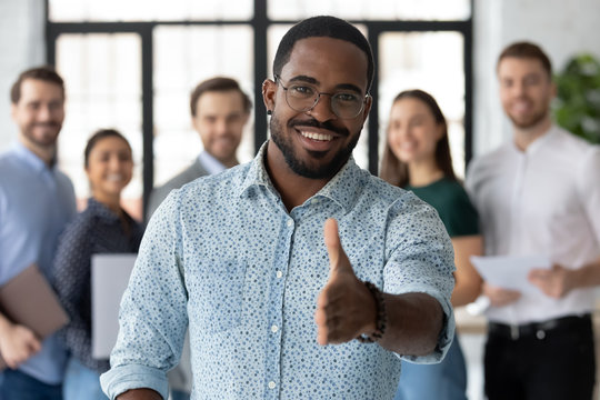 Smiling African American male employer in glasses stretch hand welcome new employee or intern in office, happy biracial boss or businessman meet greet newcomer at workplace, employment concept