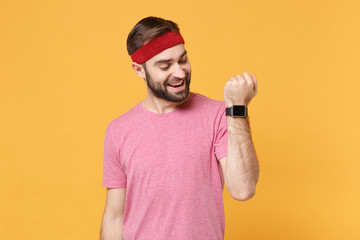 Cheerful young bearded fitness sporty guy sportsman in headband t-shirt spend weekend in home gym isolated on yellow background. Workout sport motivation lifestyle concept Wearing smart watch on hand.