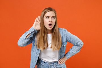 Curious young woman girl in casual denim clothes posing isolated on orange wall background studio...