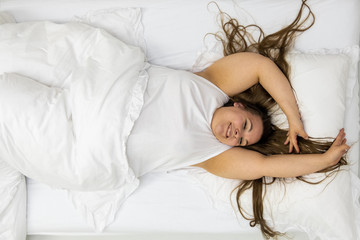 Portrait of a happy excited confident positive cheerful plump woman with dark hair in bed. Brunette...