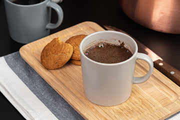 Cup of hot coffee on wooden board on kitchen table close up