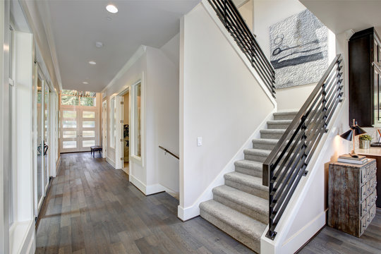 Hallway features a staircase with gray carpet runner. Luxury American modern home.