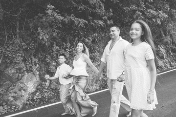 Cheerful, happy family, father, mother, son and daughter enjoying walk play outdoor. Lifestyle concept. Family in white clothes on walkway. Green forest background. Black and white.