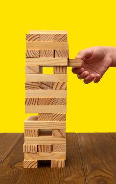 Board game geng or tower on a wooden table and a yellow background. Children's hand draws a detail of the game.