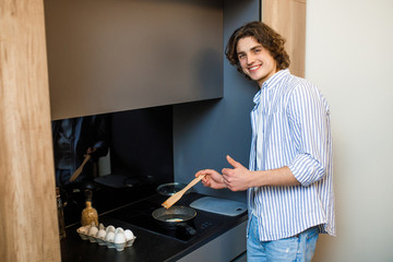 Portrait of handsome male cooking omelette use frying pan at his modern kitchen