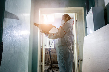 virologist in protective hazmat suit conducts disinfections of surfaces in public and isolated...