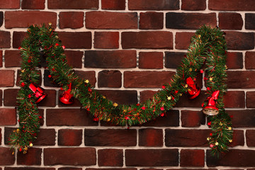 green garland with red christmas bells on a brick wall